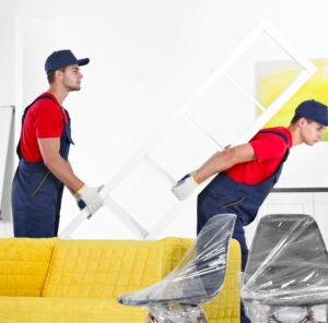 Umzug im Ruhrgebiet Zwei Helfer tragen ein Möbelstück an einem gelben Sofa vorbei – Umzug im Ruhrgebiet