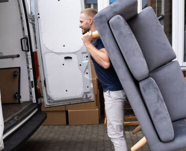 Möbellift Castrop-Rauxel Möbellift Castrop-Rauxel: Helfer tragen ein graues Sofa aus einem Transporter